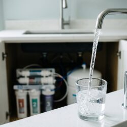 Clean drinking water flowing from a modern under-sink reverse osmosis tap in a bright kitchen, representing reverse osmosis water purification