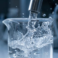 Close-up of crystal-clear deionized water flowing from a laboratory filtration system into a glass beaker, representing water purity
